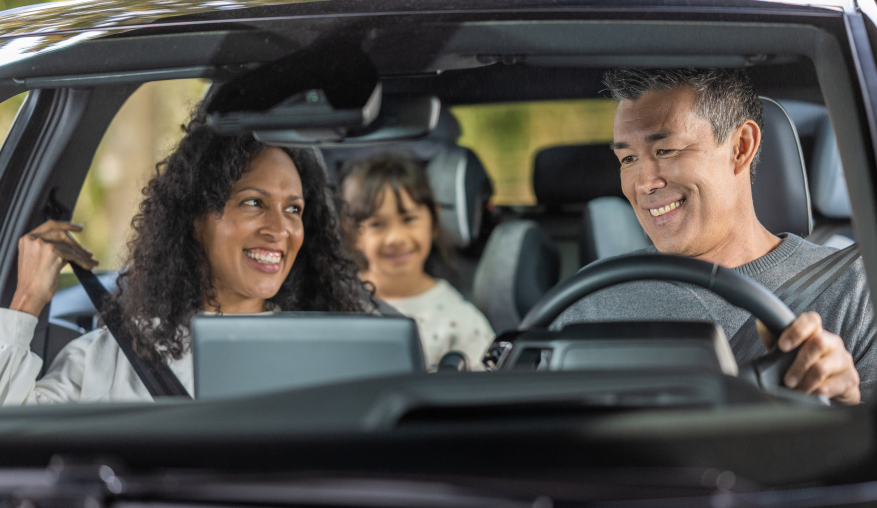 A family sitting in a passenger vehicle, smiling.