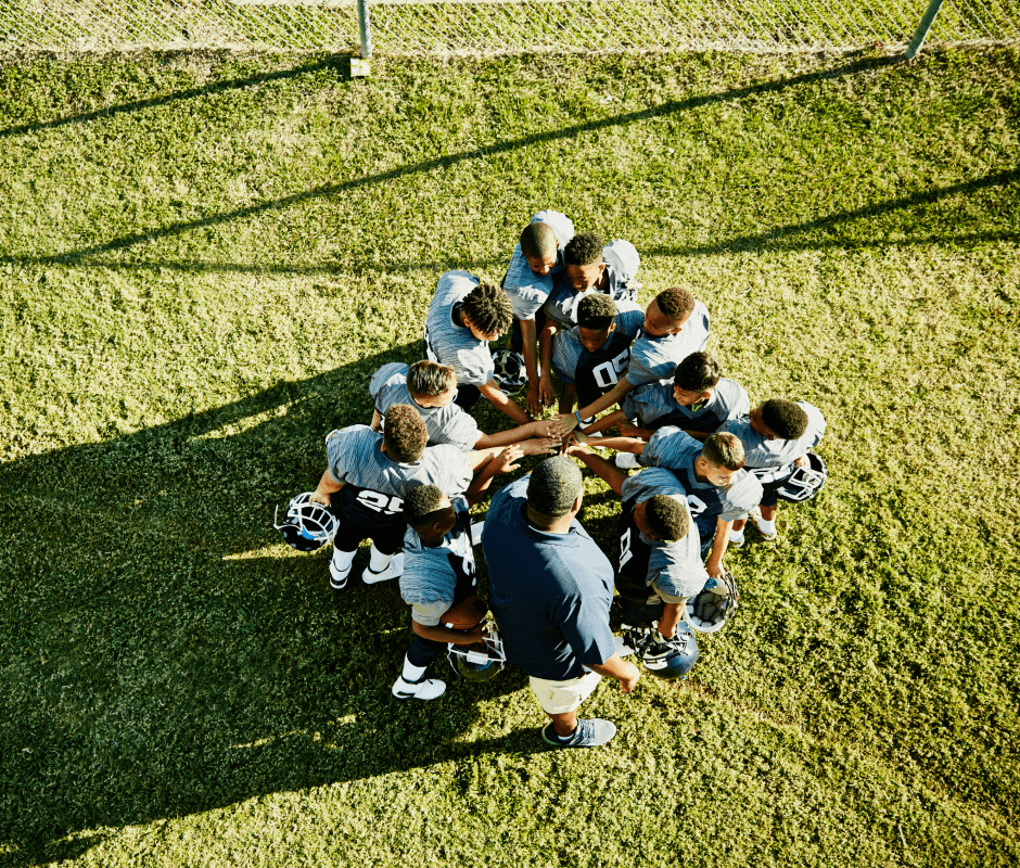 A youth football team huddles with their coach on a field.